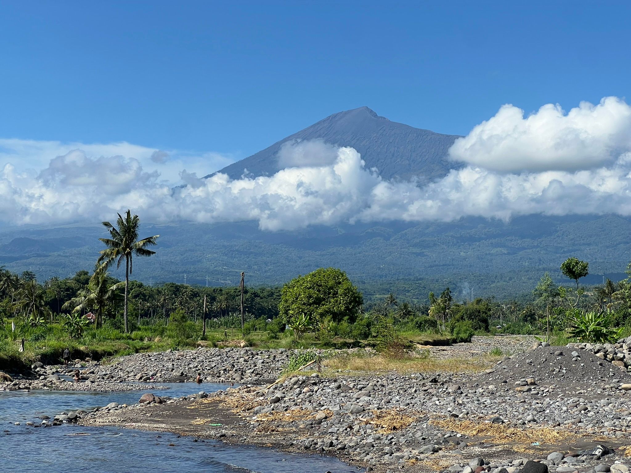 Mt. Rinjani rising over a beach between the clouds