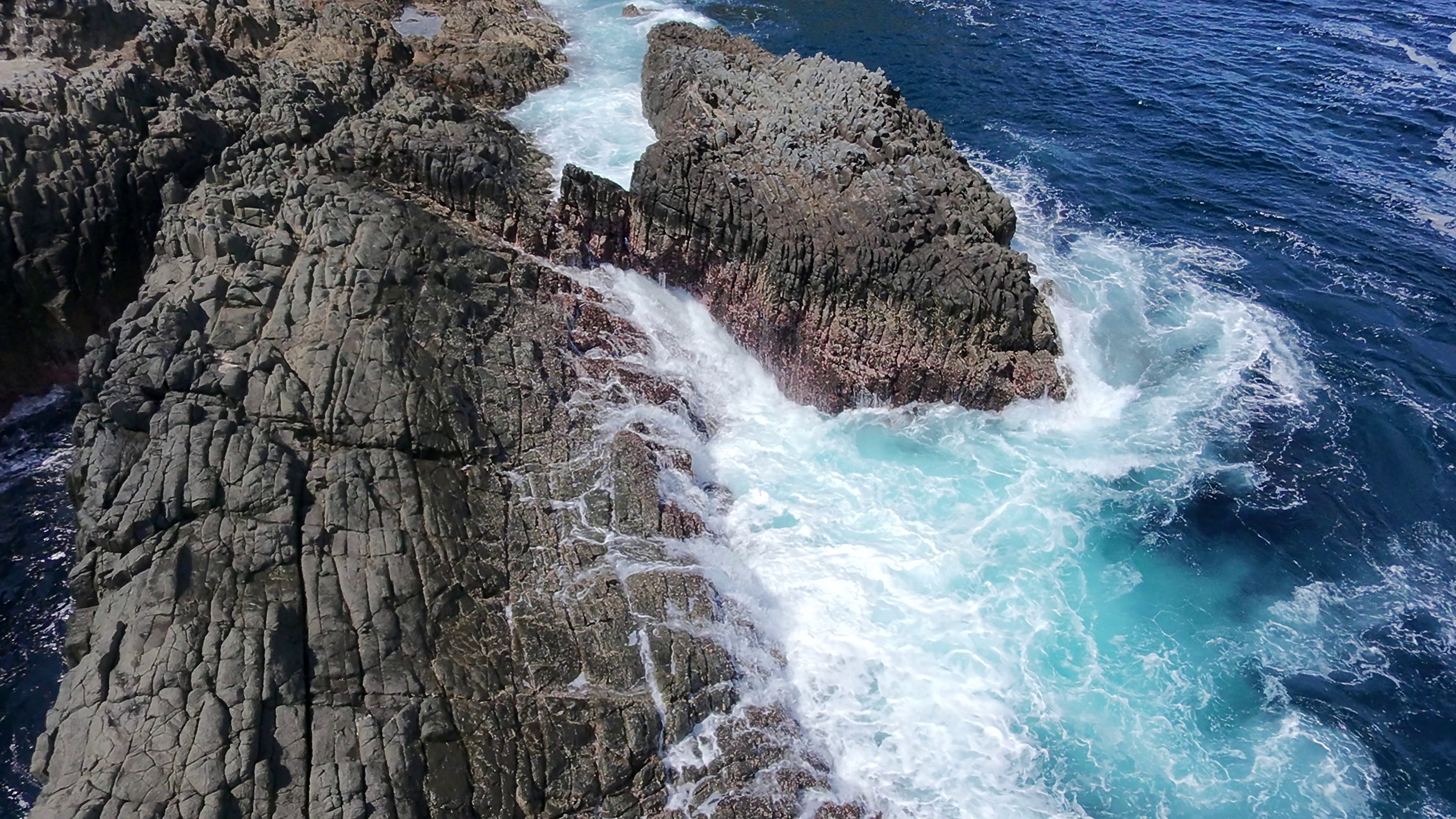 Arial view of blue waves crashing over cliffs